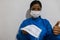 Young black woman in the medical field, with a blue gown and a face mask, offering a face mask