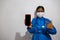 Young black woman in the medical field, wearing a blue gown and a mask that shows the screen of her phone and points