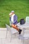 A young black woman is sitting on a chair by a green lawn, drinking coffee, taking a break