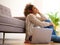 Young black woman sitting on the floor at home and listening to music with laptop and headphones