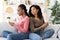 Young black women sitting back to back, using smartphones