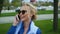 Young blond attractive woman walking in the park by the river and talking on the mobile phone. Blue shirt, business suit