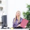 Young blond businesswoman with folder sits at the table at the office