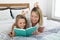 Young blond Caucasian mother lying on bed with her young sweet 7 years old daughter reading book together at home bedroom