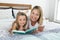 Young blond Caucasian mother lying on bed with her young sweet 7 years old daughter reading book together at home bedroom