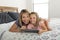 Young blond Caucasian mother lying on bed with her young sweet 7 years old daughter using internet on digital internet tablet pad