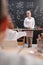 Young blond cheerful teacher of chemistry in whitecoat standing by blackboard