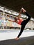 Young blond fit woman, wearing orange top, black leggings, orange sneakers, doing stretching exercise by railing on stadium.