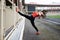 Young blond fit woman, wearing orange top, black leggings, orange sneakers, doing stretching exercise by railing on stadium.