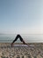 Young blond girl practice downward facing dog yoga asana on sea shore at sunrise