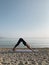 Young blond girl practice downward facing dog yoga asana on sea shore at sunrise