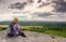 A young blond girl sit on peak and enjoy sun. Woman hiker