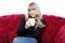 Young blond haired girl drink cup of coffee on red sofa in front