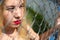 Young blond haired girl with red lips beyond the wire chain link fence looking through it
