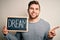 Young blond man with beard and blue eyes holding blackboard with dream message very happy pointing with hand and finger to the