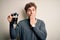 Young blond man with curly hair making coffee using coffemaker over white background cover mouth with hand shocked with shame for