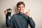 Young blond man with curly hair making coffee using coffemaker over white background happy with big smile doing ok sign, thumb up