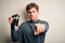 Young blond man with curly hair making coffee using coffemaker over white background pointing with finger to the camera and to