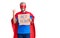 Young blond man wearing super hero costume holding act now cardboard banner screaming proud, celebrating victory and success very