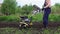 Young blond muscular farmer cultivates ground soil with rotary mini tiller.