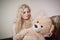 Young blond sensual woman sitting on sofa relaxing with a huge teddy bear