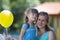 Young blond smiling happily mother hugs lovingly and protectively her small pretty preschool daughter girl with bright balloons o