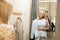 Young blond smiling woman trying white sweatshirt in front of mirror