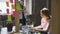 Young blond student wearing casual clothes is busy typing on laptop while her friend is reading book standing near