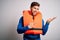 Young blond tourist man with beard and blue eyes wearing lifejacket over white background amazed and smiling to the camera while