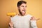 Young blond vegetarian man with beard and blue eyes holding fork with fresh cob corn pointing and showing with thumb up to the