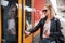 Young blond woman in jeans, shirt and leather jacket wearing bag and sunglass, presses door button of modern speed train