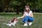 Young blond woman, kneeling down, holding her dog`s paw in park in summer. Dog owner training her Cavalier king charles spaniel