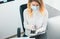 Young blond woman manager in medical protection mask and gloves types message in smartphone working in office during Covid-19