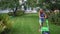 Young blond woman mowing lawn in residential back garden on summer evening