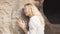 A young blond woman with a pretty face leaned against the rocks of the ancient city Uplistsikhe. The girl listens to the