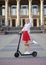 Young blond woman, riding on black electric scooter in city center in front of old historical building with pillars. Summer