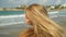 Young blond woman shakes her head, making her blond hair fluttering on the sea background in slow motion. Lonely girl
