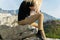 Young blond woman sitting on the edge of the mountain cliff using the smartphone