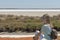 Young blond woman sitting on the rock next to colorful salt lagoon in Camargue Nature Park, Southern France