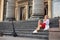Young blond woman, sitting on staircase of old historical building with pillars in city center. Female portrait with electric