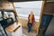 Young blond woman standing next to camper van overlooking the sea