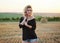 Young blond woman, wearing black jacket and jeans shorts, posing on wheat field on summer evening. Creative stylish three-quarter