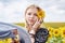 Young blond woman, wearing boho hippie clothes, holding grey transparent shawl scarf, waving on wind on yellow sunflowers field.