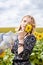 Young blond woman, wearing boho hippie clothes, holding grey transparent shawl scarf, waving on wind on yellow sunflowers field.