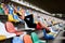 Young blond woman, wearing orange top, black leggings, orange sneakers, lying with her legs up on colorful seats on stadium,