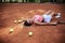 Young blond woman, wearing pink top, white skirt and sneakers, lying on orange ground on tennis court, holding racket with light