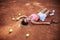 Young blond woman, wearing pink top, white skirt and sneakers, lying on orange ground on tennis court, holding racket with light