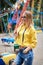 Young blond woman, wearing yellow hoody and blue jeans, holding colorful sweet tasty lollypop in amusement theme park. Three-