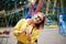 Young blond woman, wearing yellow hoody and blue jeans, holding colorful sweet tasty lollypop in amusement theme park. Three-