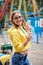 Young blond woman, wearing yellow hoody and blue jeans, holding colorful sweet tasty lollypop in amusement theme park. Three-